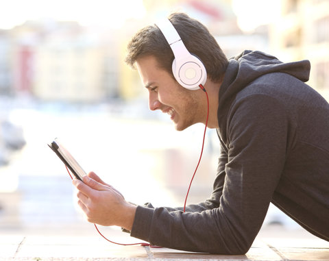 Smiling man wearing headphones while using a smartphone outside.